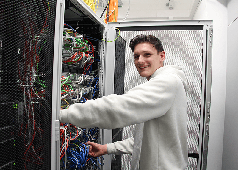 Auszubildender Fachinformatiker für Systemintegration mit weißem Pulli am Computer im Serverraum