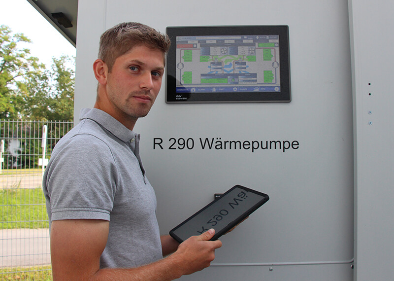 Kratschmayer Mitarbeiter steht vor einer Wärmepumpe, die mit dem natürlichen Kältemittel R290, und hält ein Tablet in der Hand.
