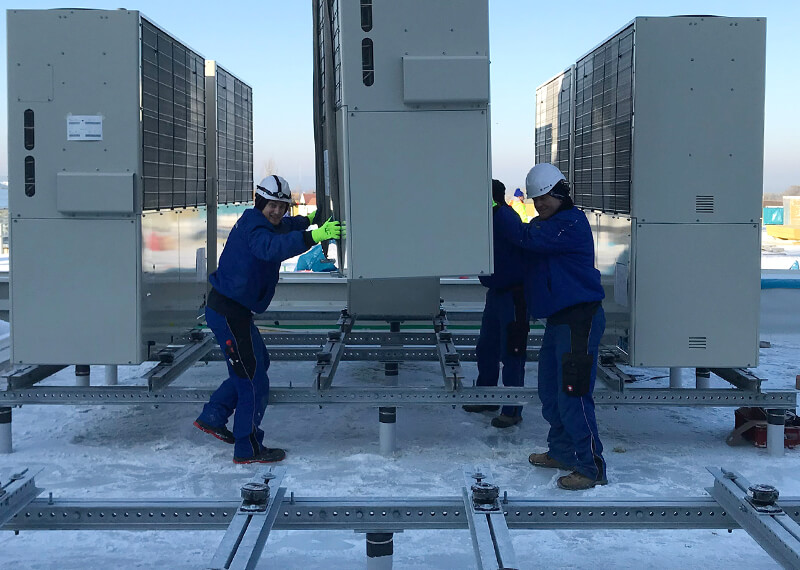 Drei Kratschmayer Mitarbeiter platzieren das Außengerät einer Klimaanlage auf dem Dach eines Kunden.