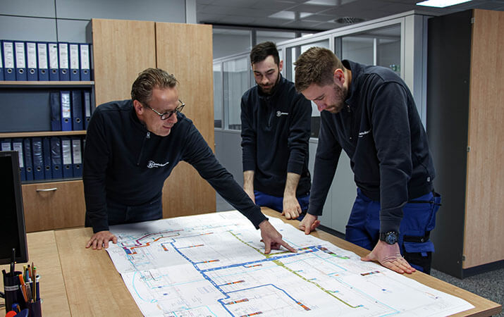 Drei Kratschmayer Mitarbeiter studieren eine Zeichnung für die Installation einer Lüftungsanlage.